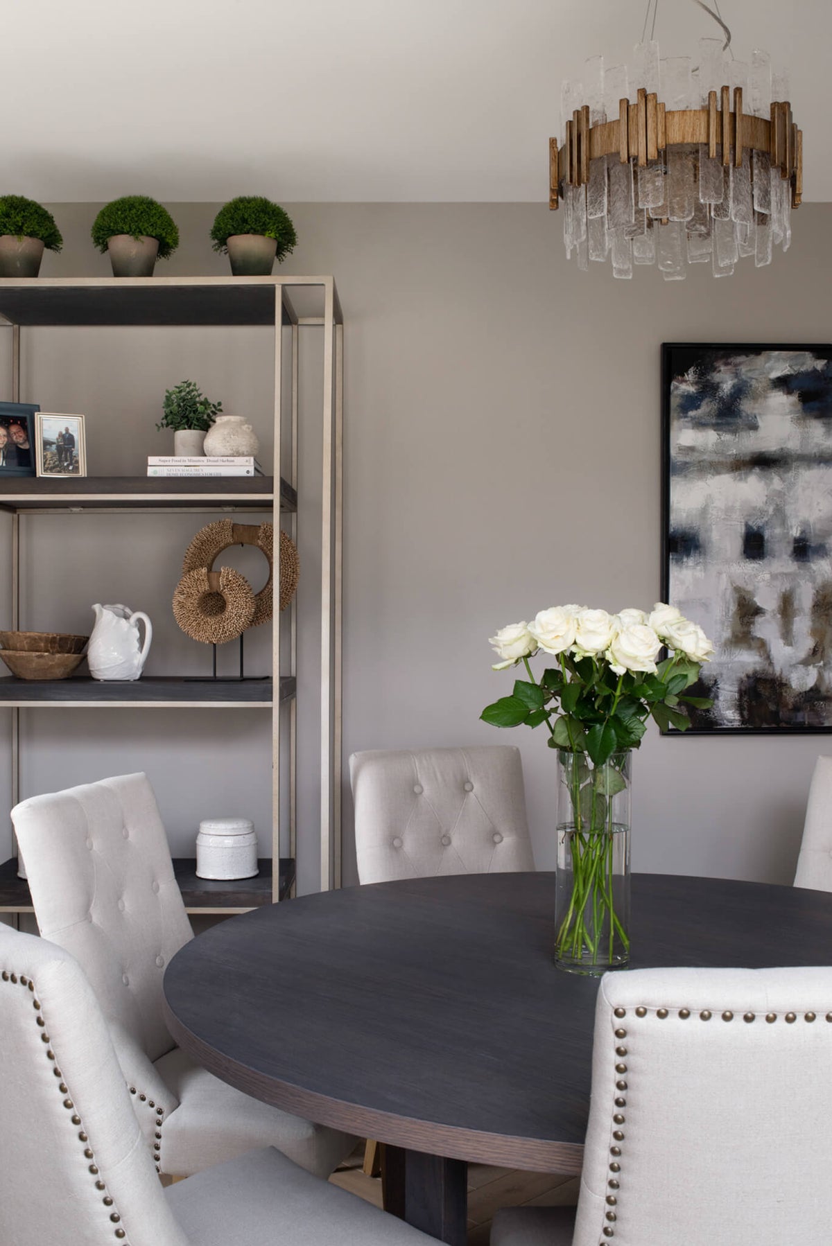 Dining area with a round table, styled open shelving and a brass pendant over white roses