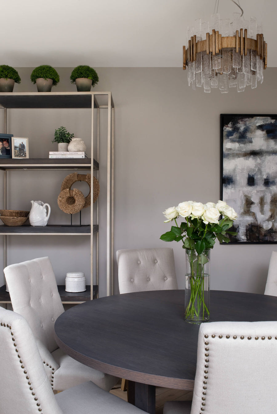 Dining area with a round table, styled open shelving and a brass pendant over white roses