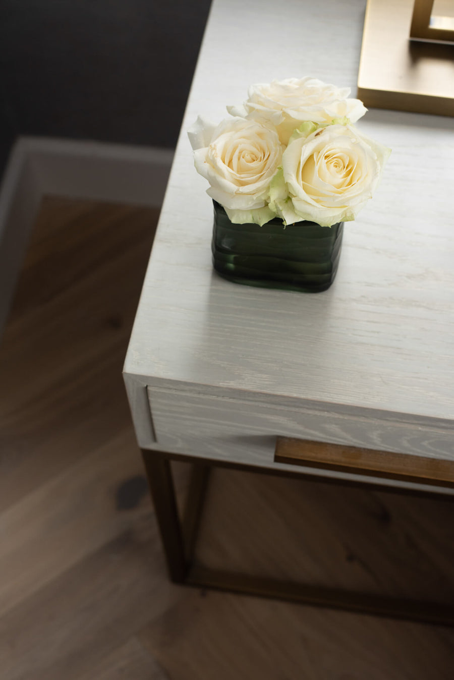 Corner of a pale oak desk with a brass tray and white roses in a glass vase