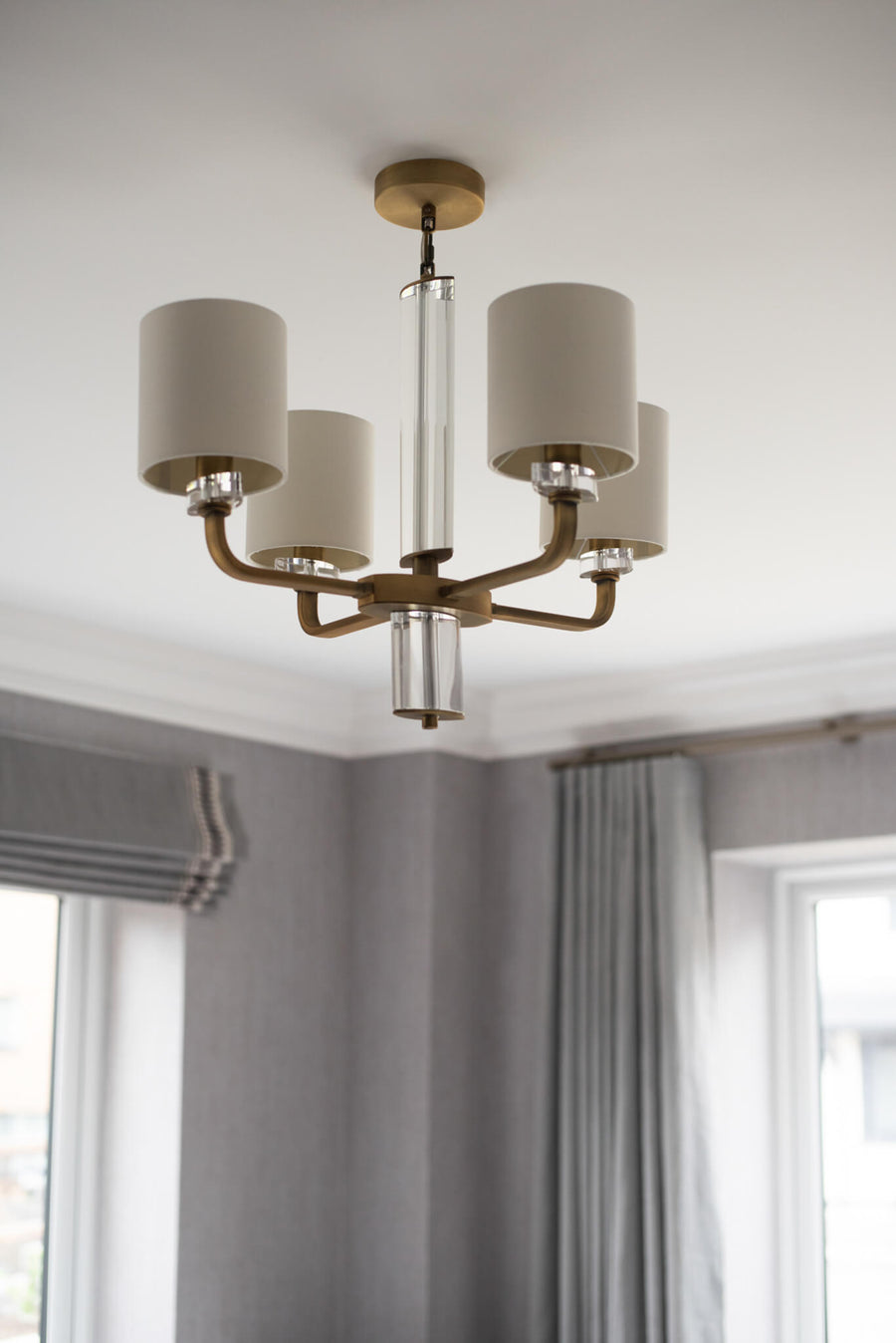 Five-arm brass chandelier with cream shades above a grey roman blind and curtains