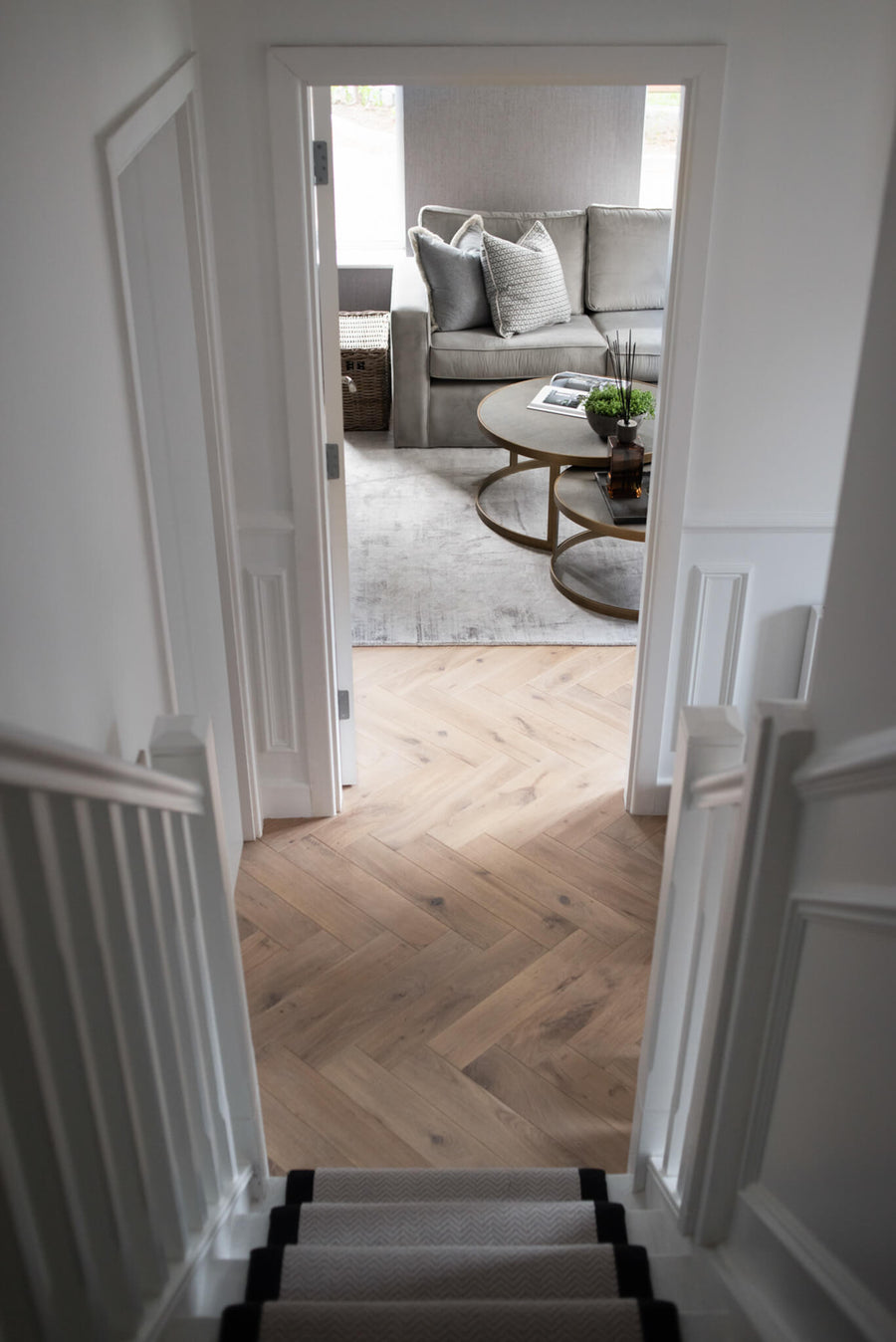 View through a panelled doorway into a living room, with a stair runner and herringbone floor