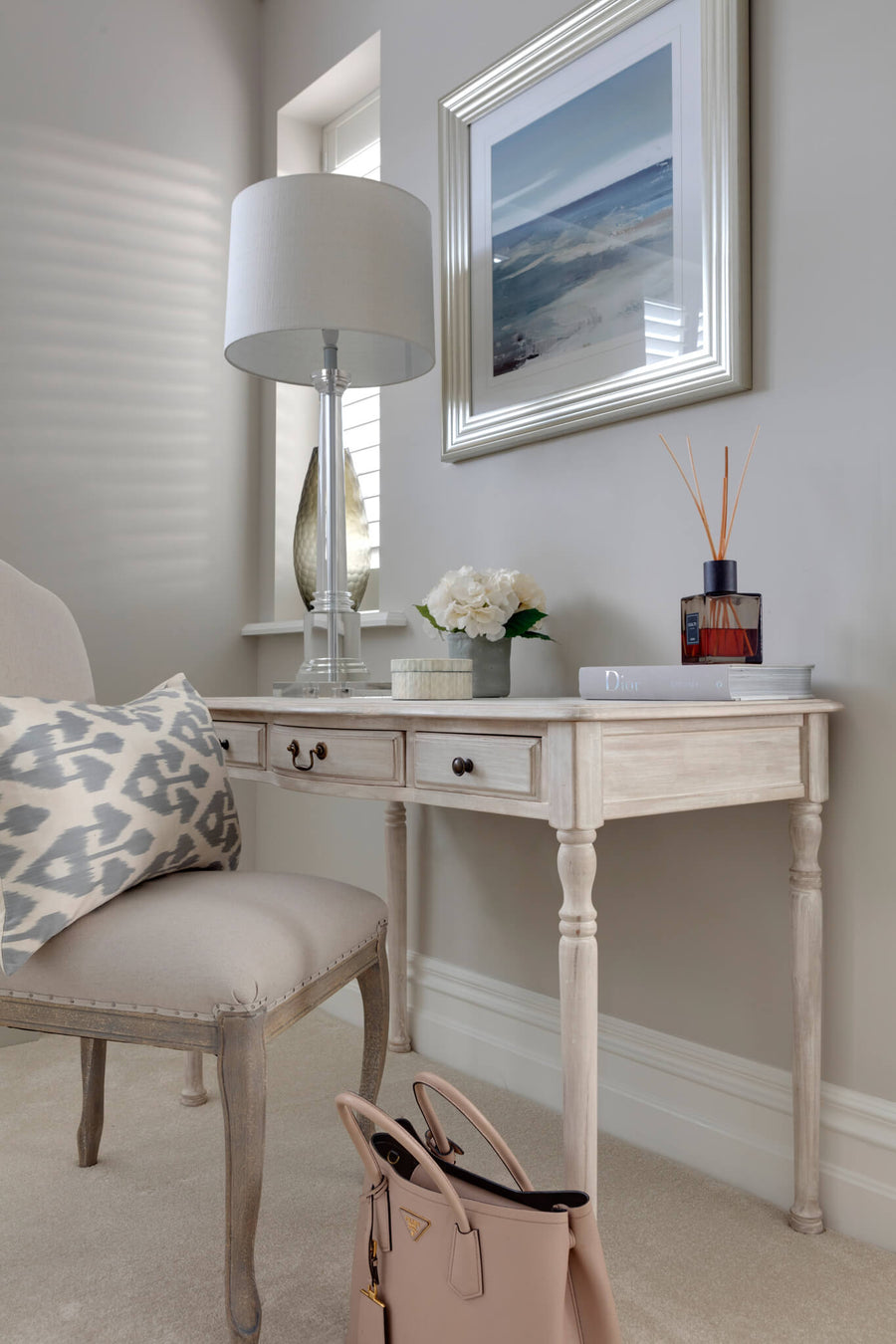 Painted dressing table with a table lamp, upholstered chair and a coastal artwork