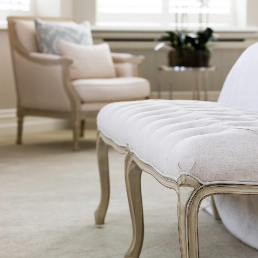 Detail of a buttoned linen bench with carved painted legs on a pale carpet
