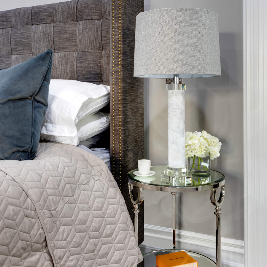 Bed with a woven leather headboard, blue velvet cushions and a mirrored side table