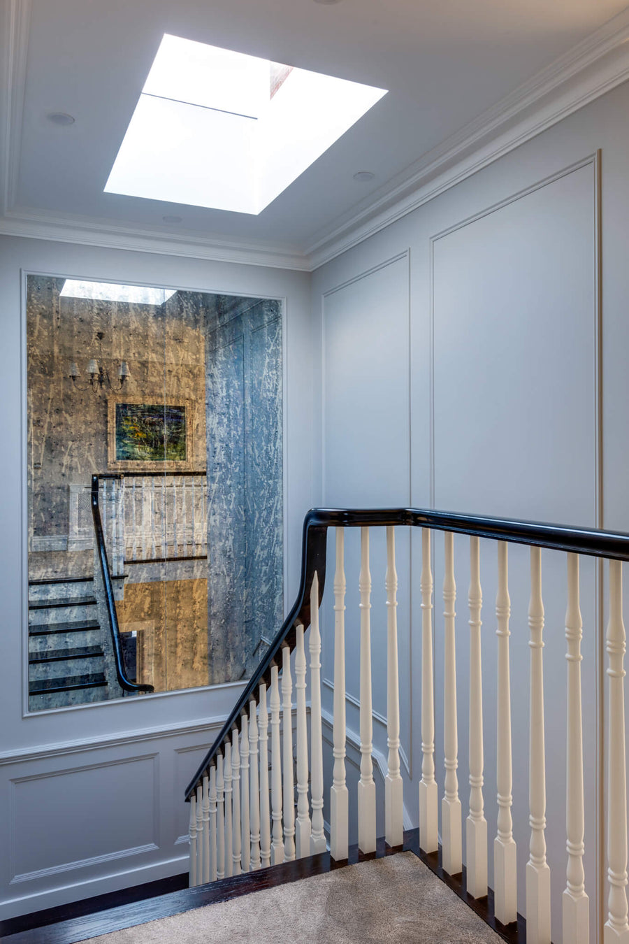 Stairwell lit by a rooflight, with a curved balustrade and a textured artwork