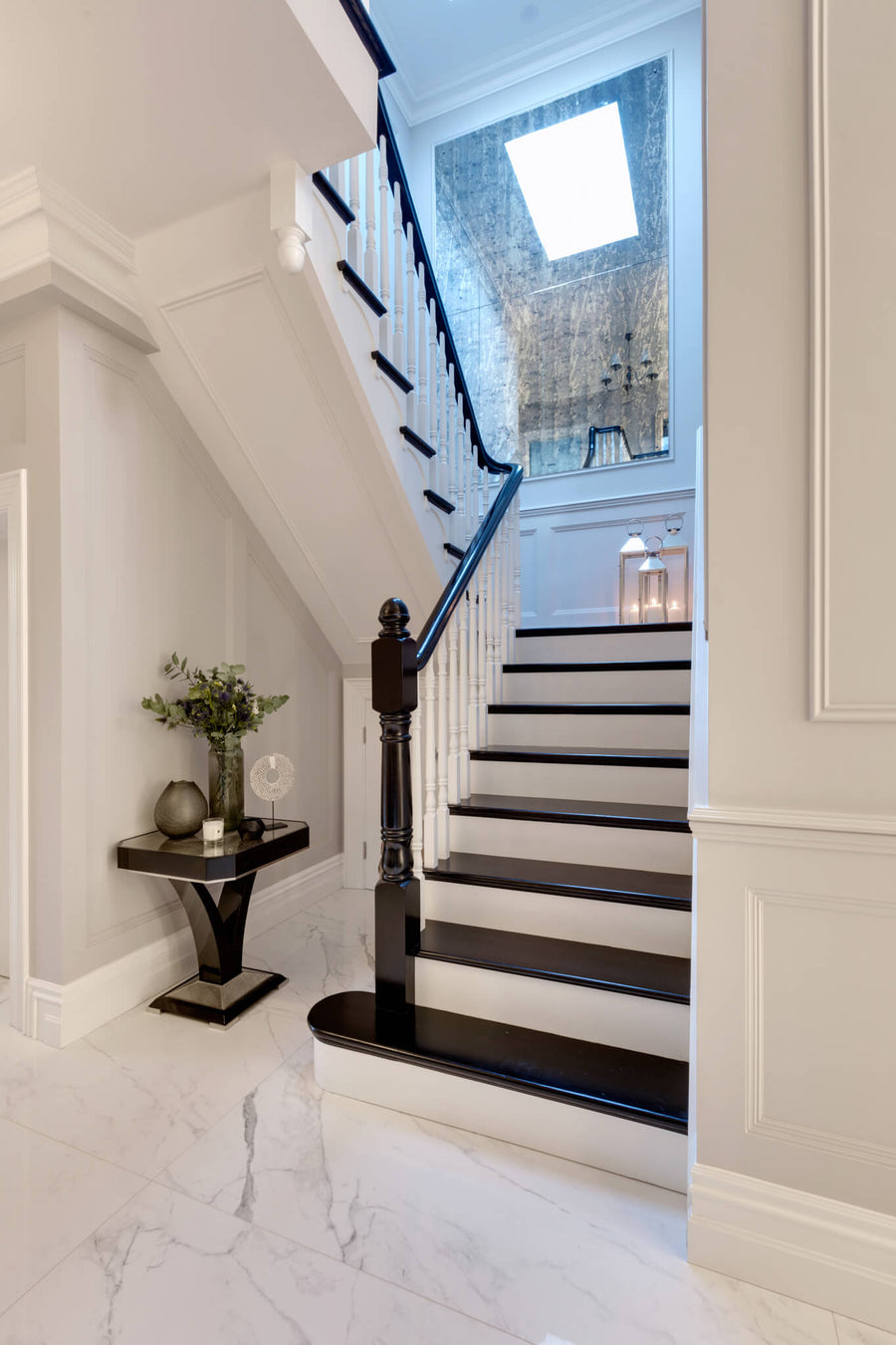 Hallway with a marble floor, a dark timber staircase and a console styled with foliage