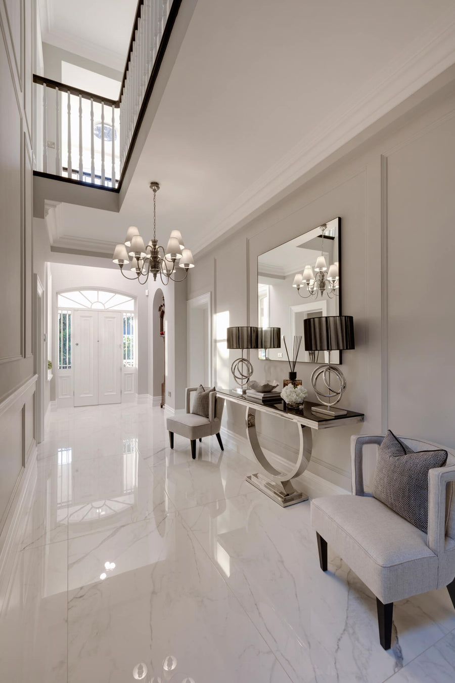 Double-height hallway with a polished marble floor, a mirrored console and a crystal chandelier