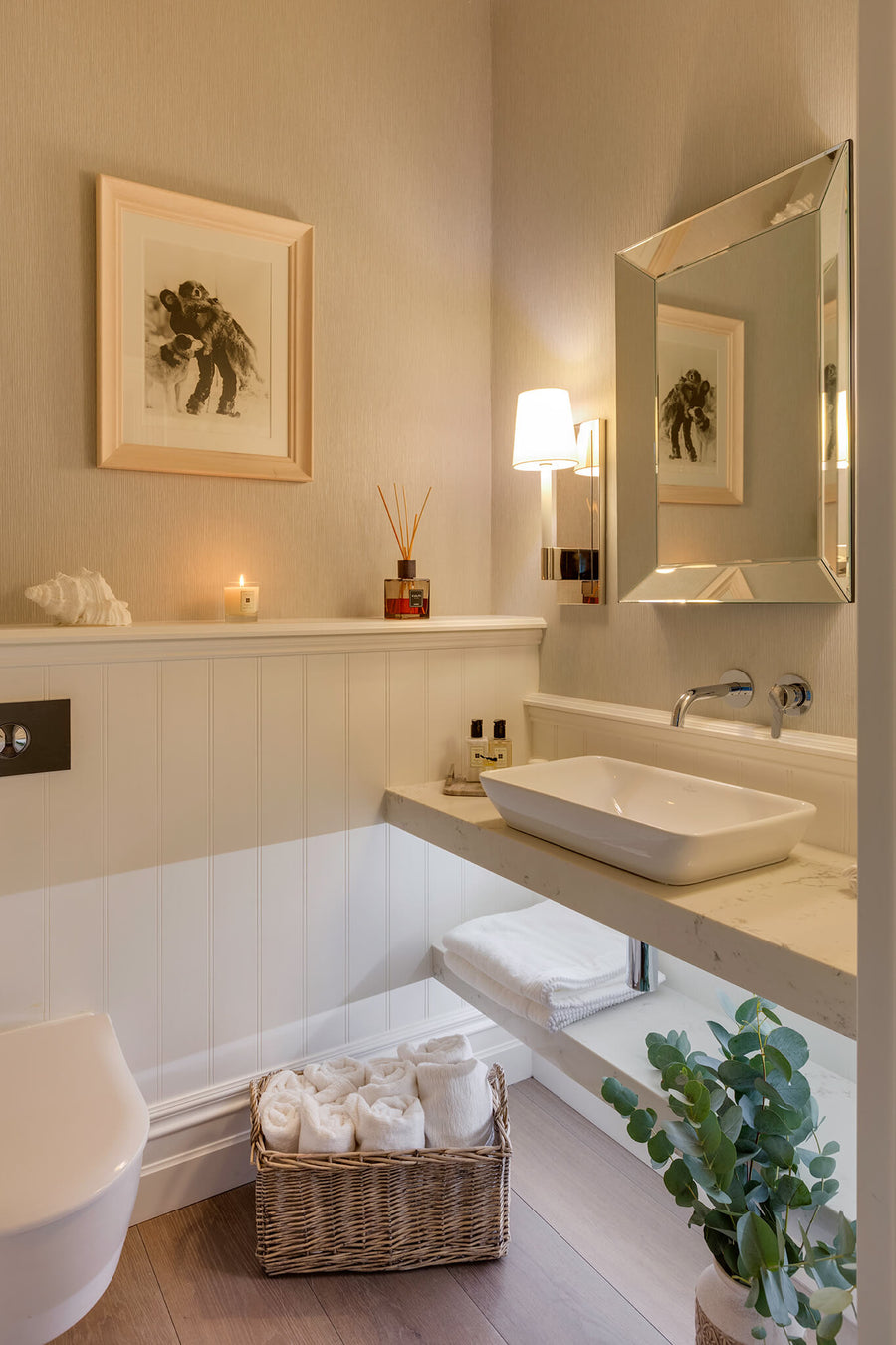 Panelled cloakroom with a vessel basin, framed botanical prints and a bath with folded towels