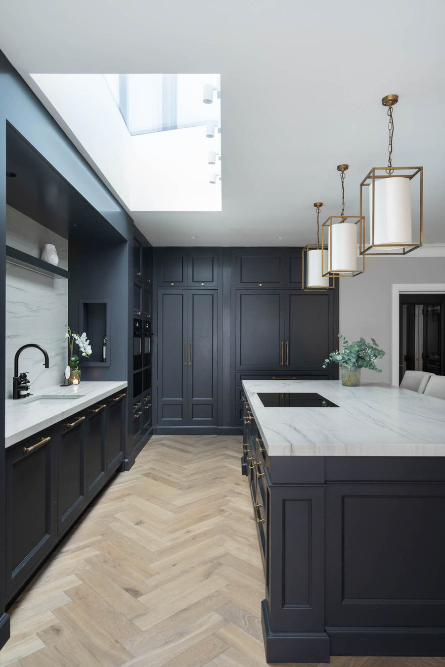 Navy kitchen with herringbone flooring, a marble-topped island and lantern pendants