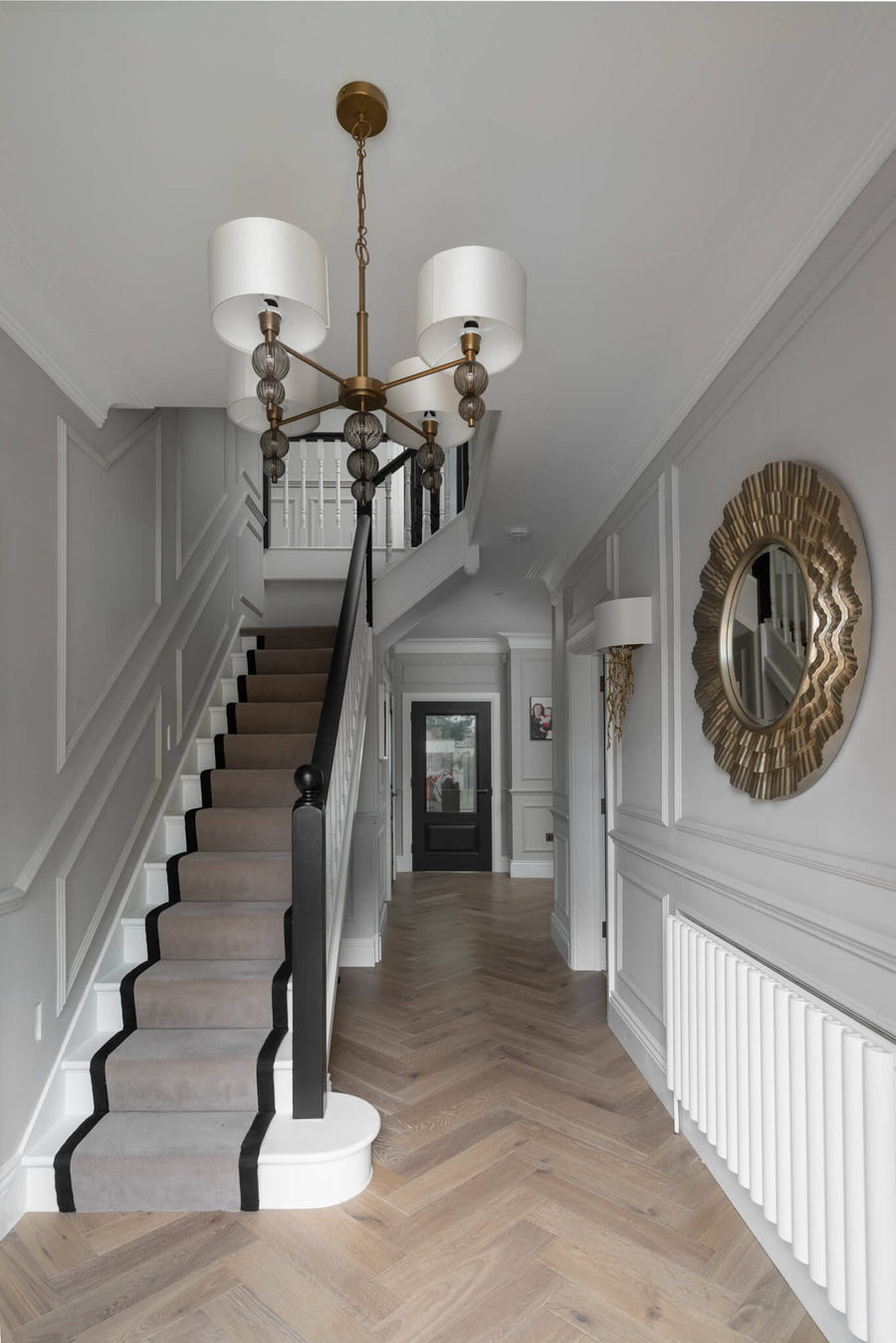 Hallway with a chandelier, sunburst mirror, panelled walls and herringbone flooring