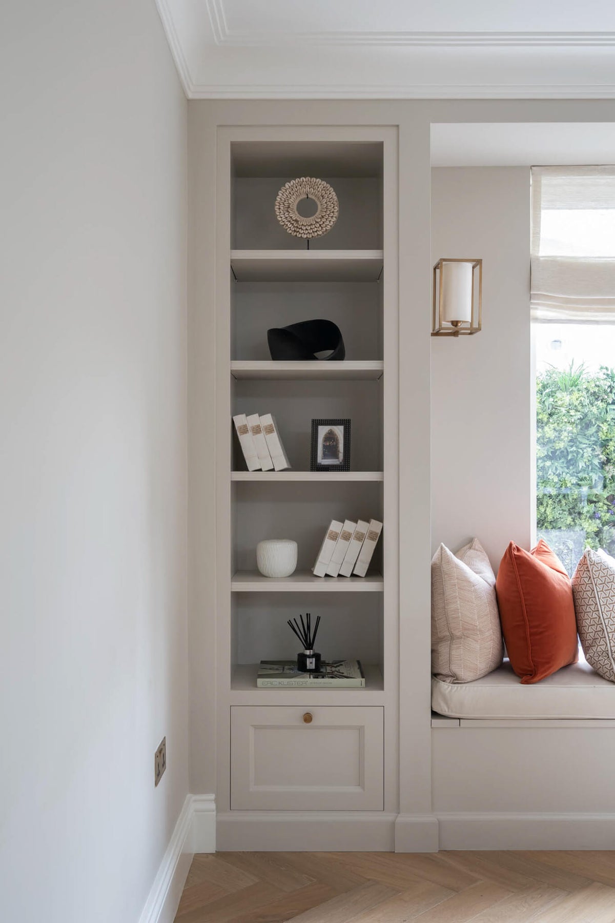 Alcove shelving beside a window seat with a rust cushion, in soft grey joinery