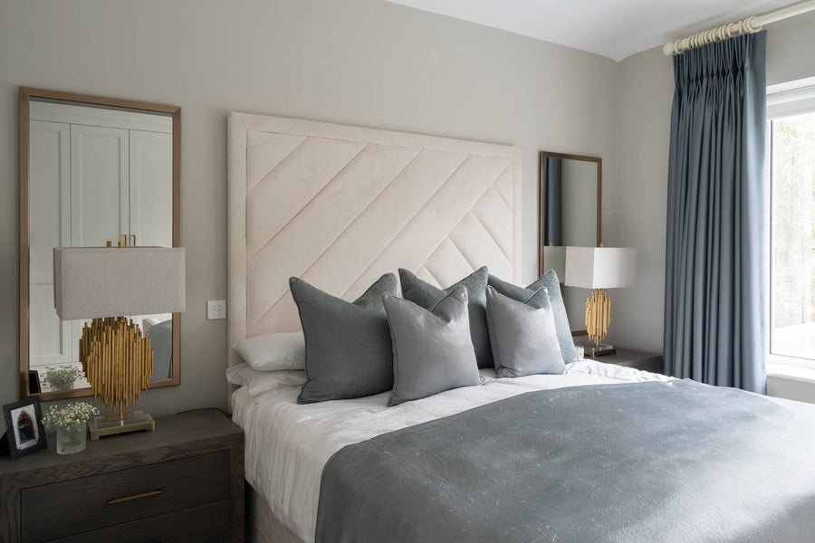 Bedroom with a cream chevron-stitched headboard, blue curtains and a pair of table lamps
