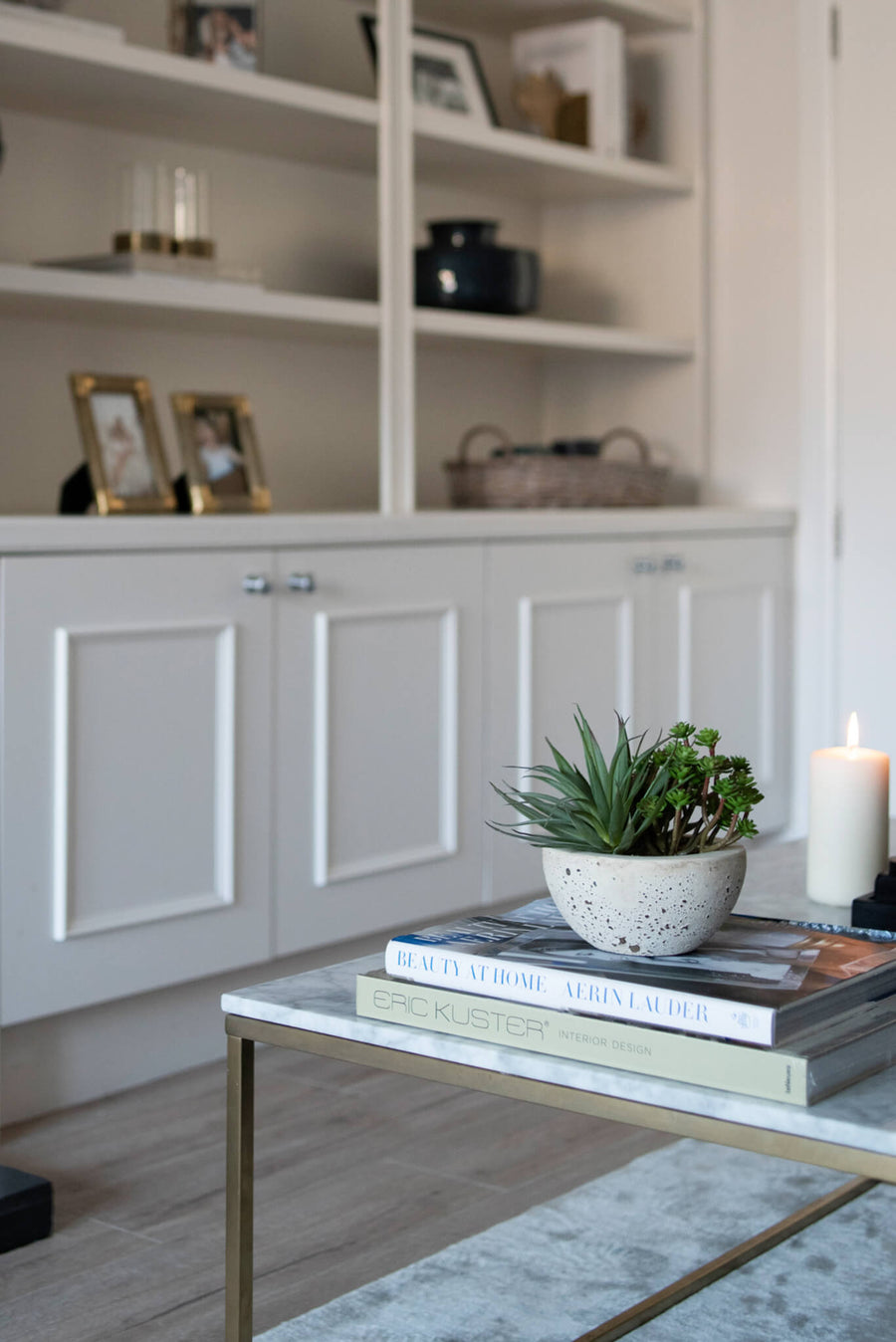 Alcove cabinetry styled with books, a candle and a succulent above a glass and brass table