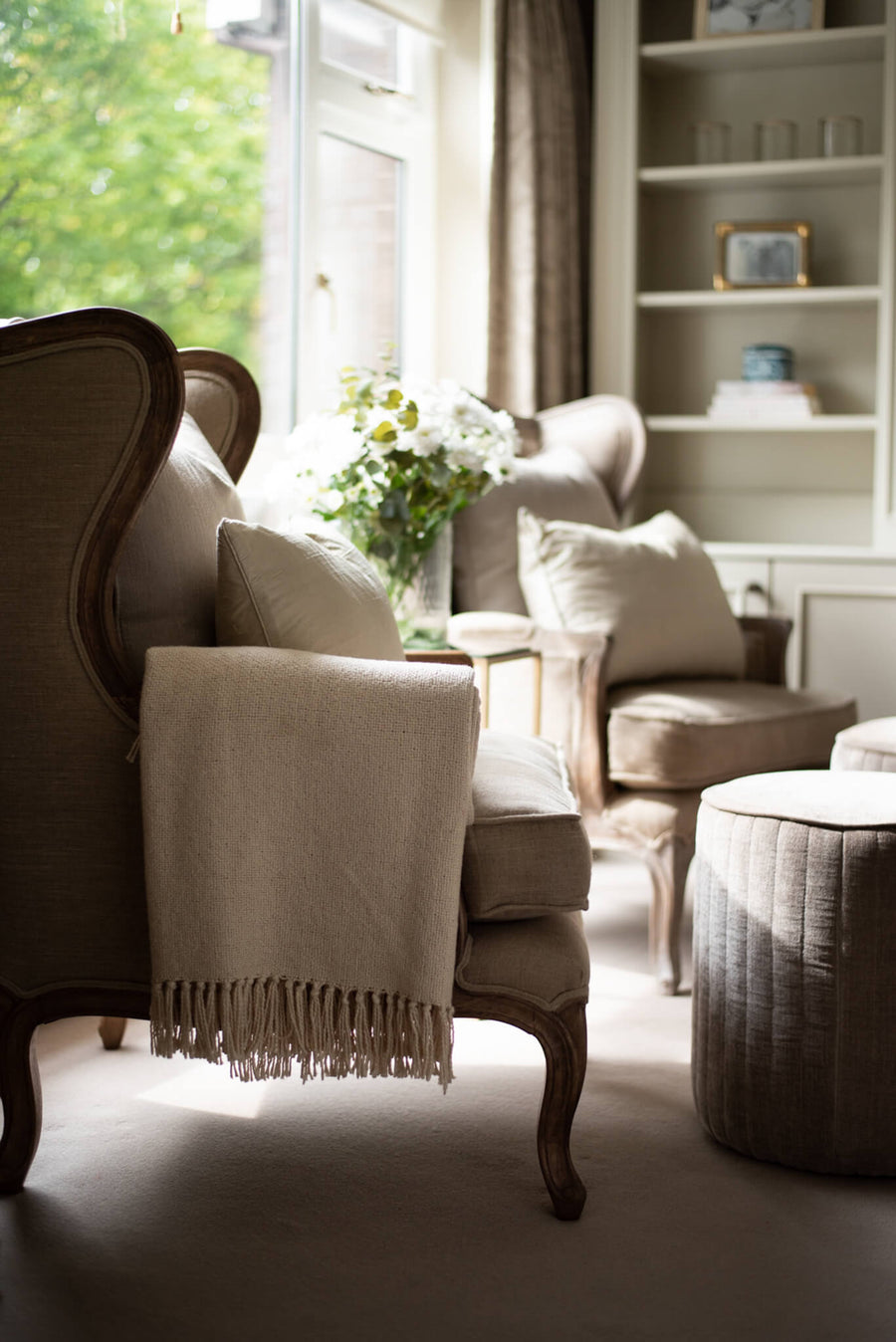 Wing armchair with a fringed throw beside a bookcase and a garden window