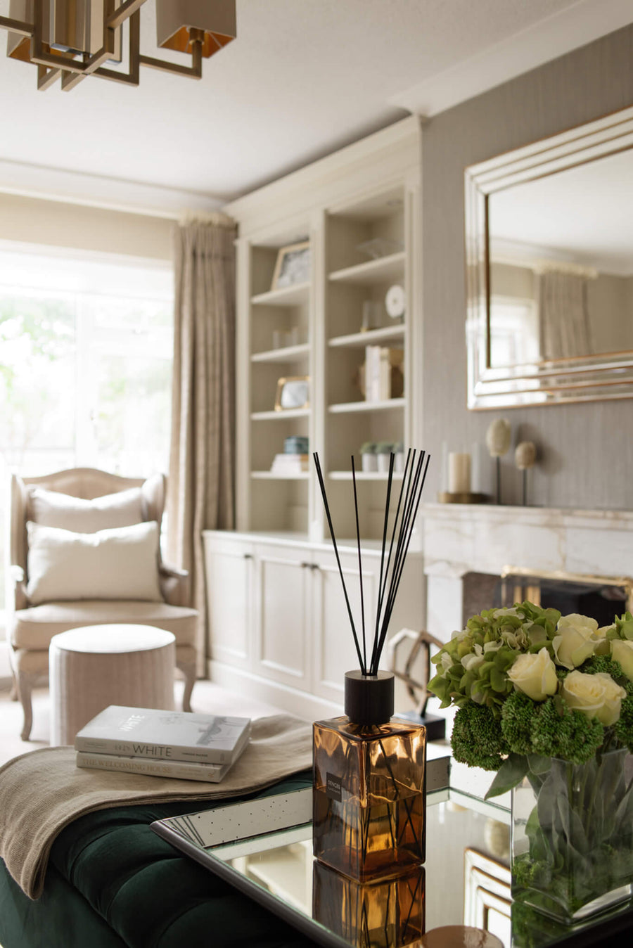 Living room vignette with a diffuser, white roses and books on a mirrored table