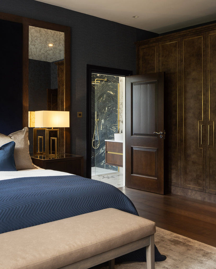 View from a navy bedroom through to a marble ensuite, with dark timber wardrobes and an antiqued mirror