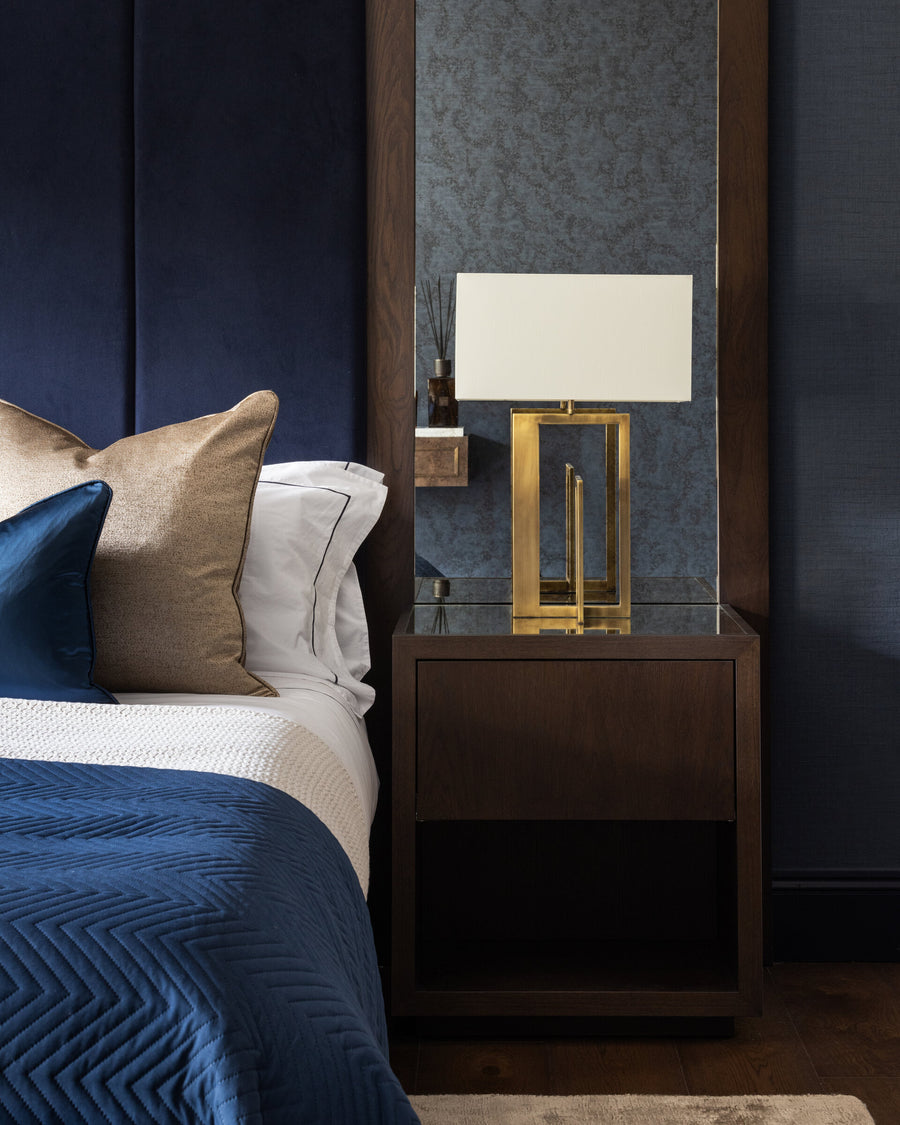 Dark timber bedside table with a brass and linen-shaded lamp against a navy panelled wall