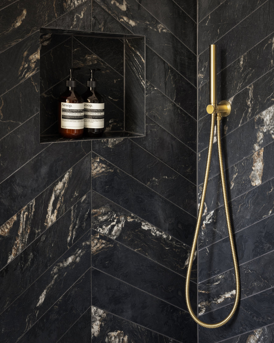 Chevron-laid black marble shower wall with brushed brass fittings and a recessed niche