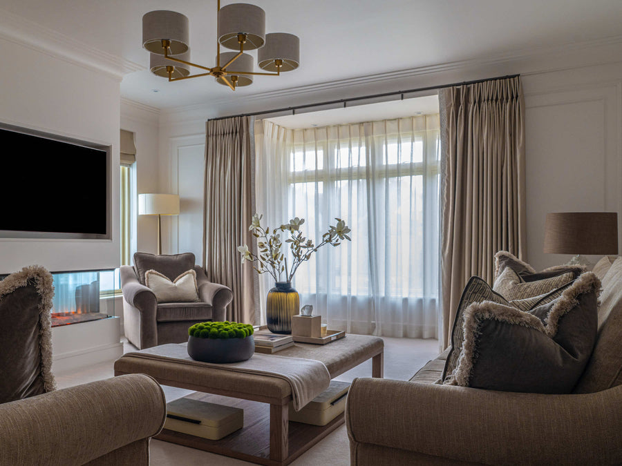 Living room with panelled walls, a brass chandelier and layered neutral seating around a low timber coffee table