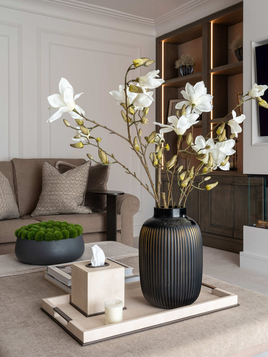 Coffee table styled with white magnolia stems in a ribbed black vase, a moss bowl and a linen tray