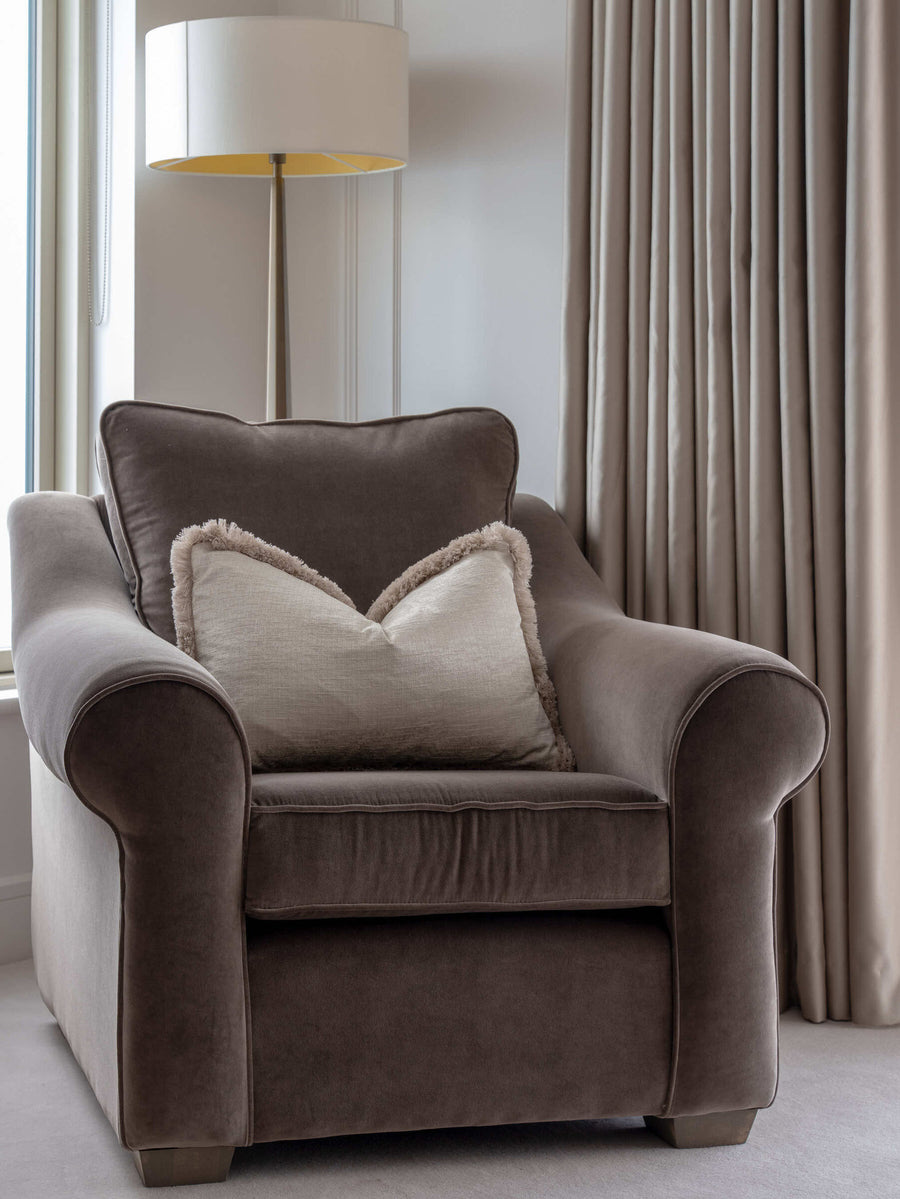 Deep brown velvet armchair with a soft linen cushion against a panelled wall